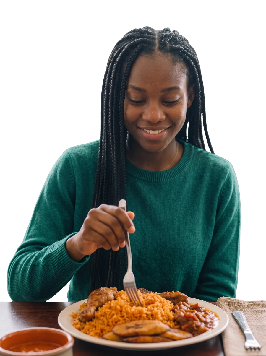 A woman smiling while eating a plate of jollof rice, chicken, and fried plantain